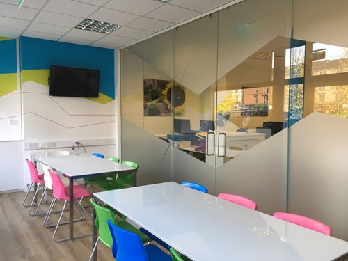 View from inside a break room with tables and chairs beside glass partitions for office